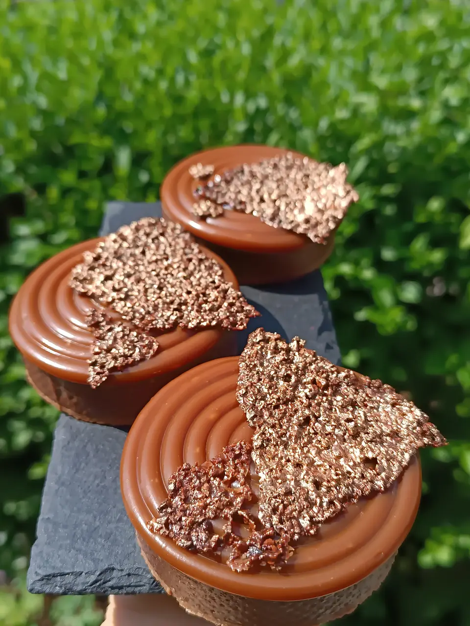 Three chocolate-coloured tartlets with smooth spiral piping and textured decorations on a slate board