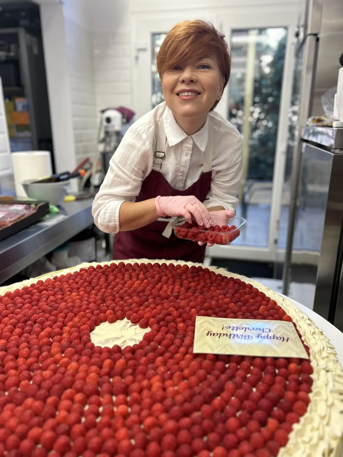 Tanya Novak smiling while finishing a raspberry cake in the Art Bakery kitchen