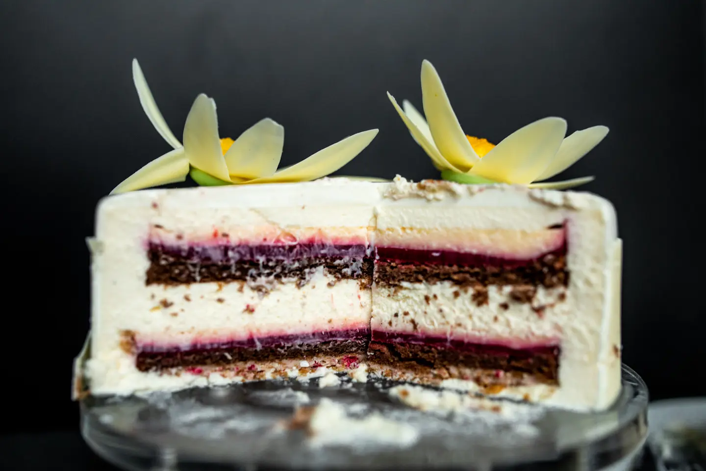 Cut cake showing dark red bands between pale cream and brown sponge, topped with flower-shaped decorations