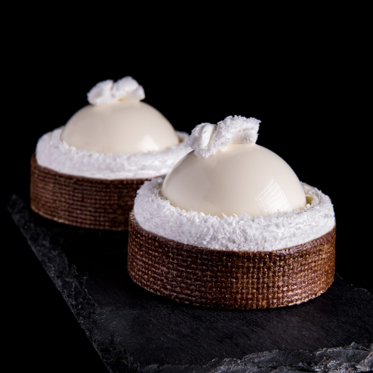 White coconut dome pastries in dark textured shells with coconut decoration