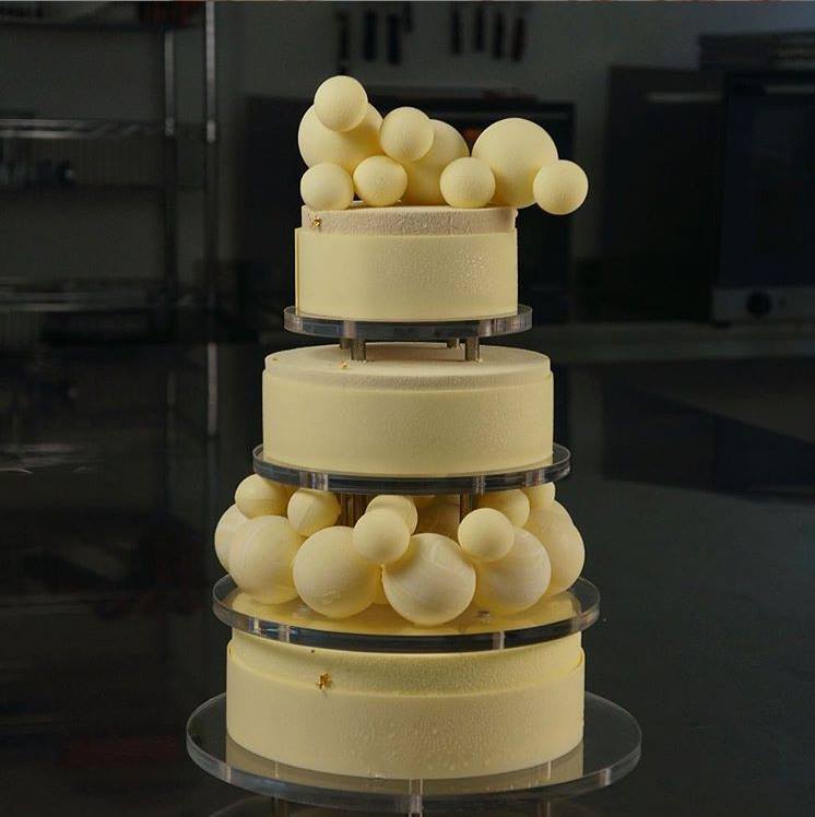 Three-tier ivory wedding cake with white chocolate spheres and clear separators