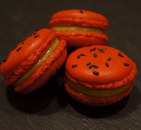 Red-orange macarons with black sesame and pale citrus cream