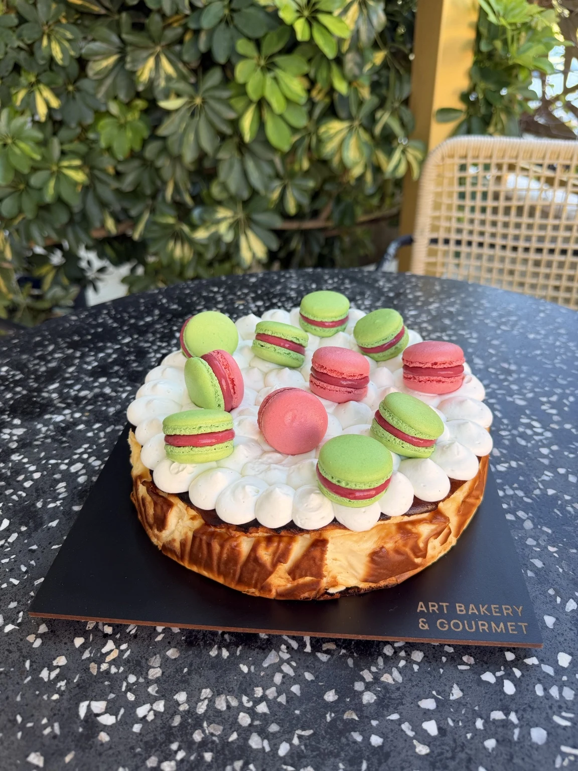 Cheesecake with piped vanilla cream and pink and green macarons at Art Bakery & Gourmet