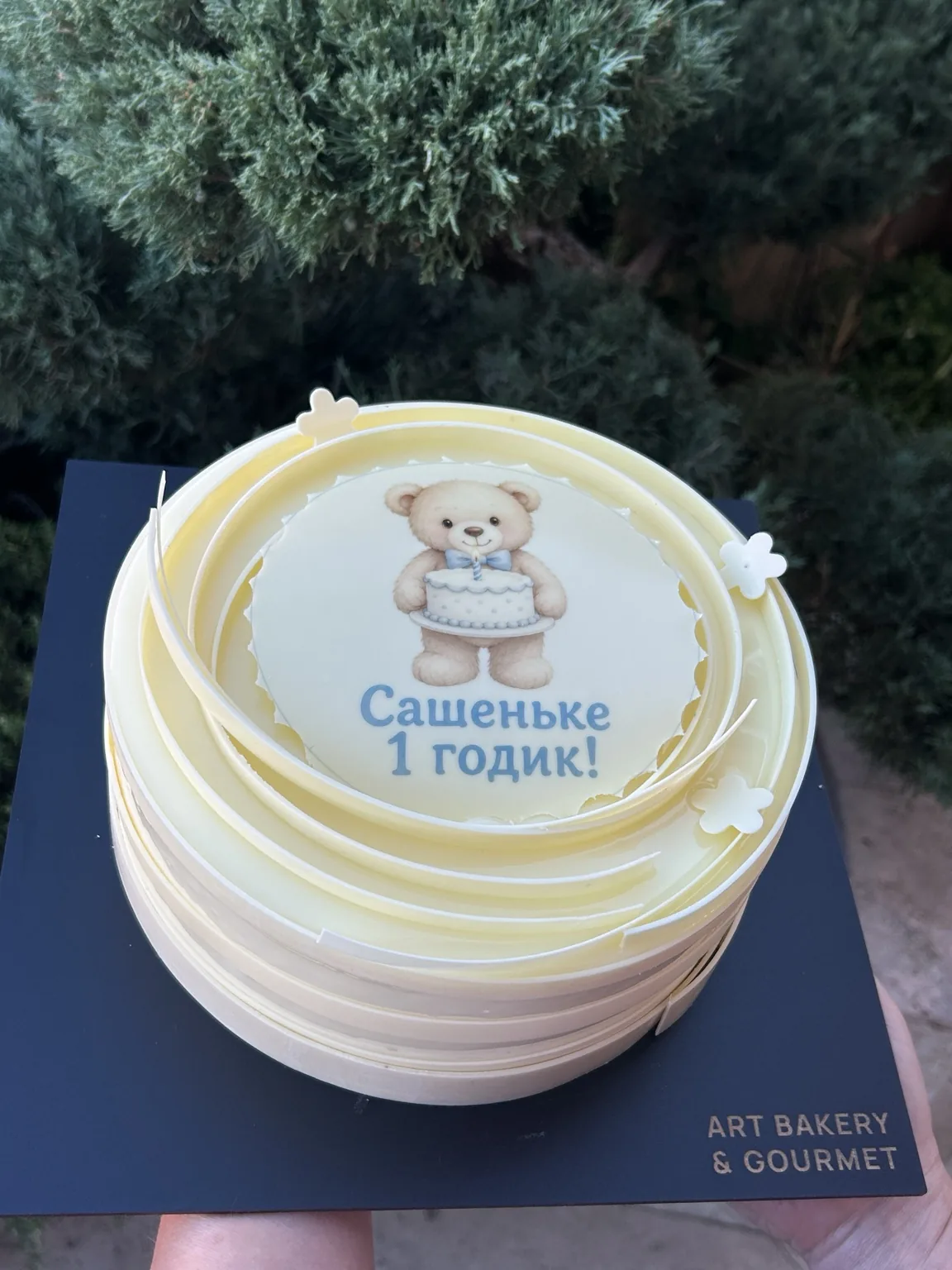 Children’s first birthday cake by Tanya Novak with pastel decoration, a teddy bear illustration and a personalised message