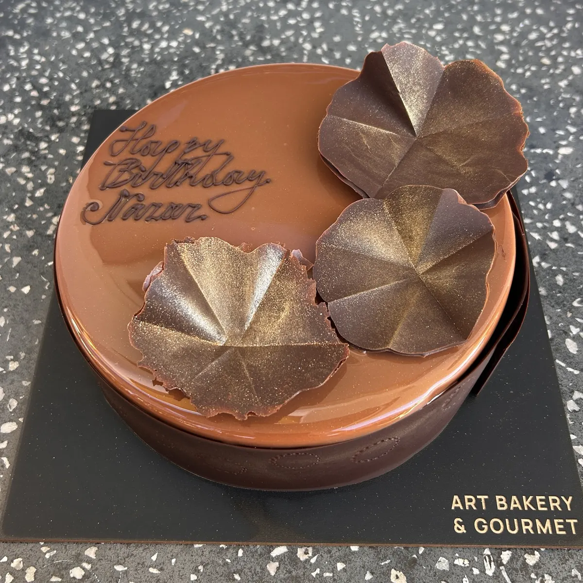 Gluten-Free Valrhona Chocolate Cake with chocolate glaze, gold-dusted chocolate leaves and birthday writing at Art Bakery & Gourmet
