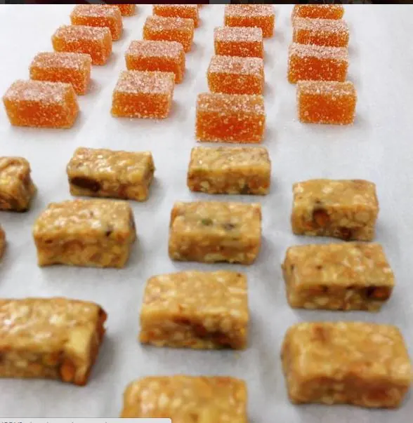 Sugar-coated orange fruit jelly cubes beside small nut confections