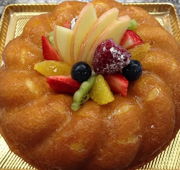 Glossy ring-shaped savarin topped with sliced apple, berries and citrus fruit